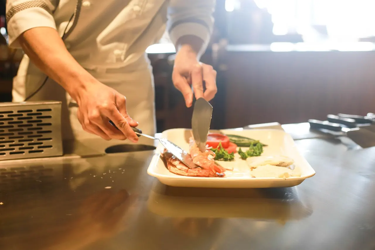 Chef preparing a plate on a steel prep counter in a restaurant kitchen